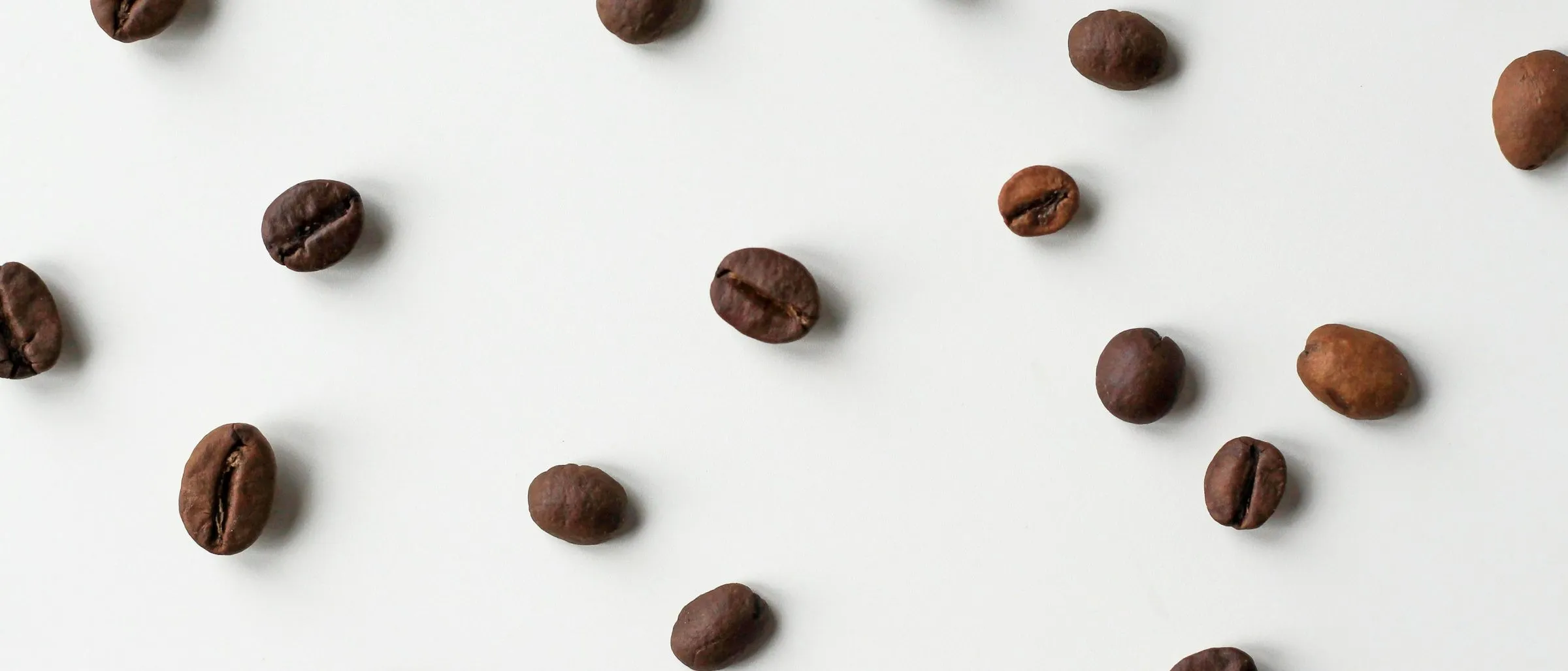 Roasted coffee beans scattered on a plain white surface.