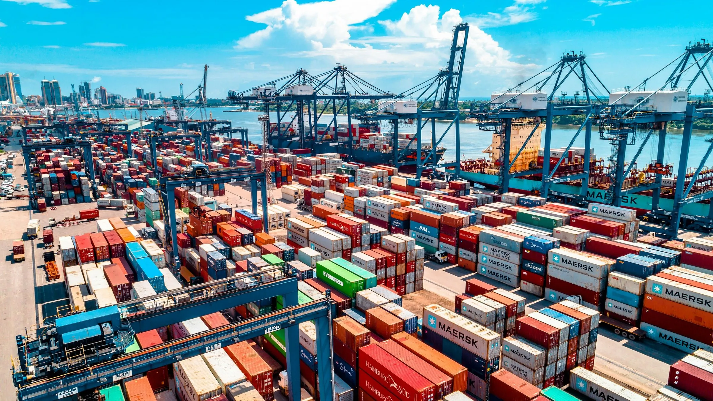 A container port with stacked shipping containers and gantry cranes.